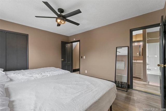 bedroom featuring a textured ceiling, ensuite bath, wood finished floors, and a ceiling fan