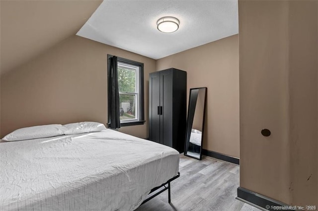 bedroom with lofted ceiling, light wood-type flooring, and baseboards