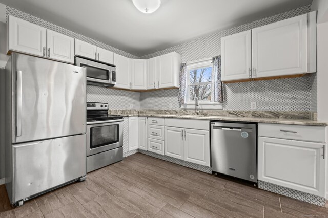 kitchen with light stone countertops, white cabinetry, a sink, stainless steel appliances, and decorative backsplash