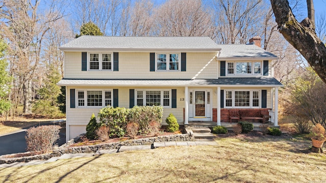 traditional-style home featuring a front lawn, an attached garage, roof with shingles, and a chimney