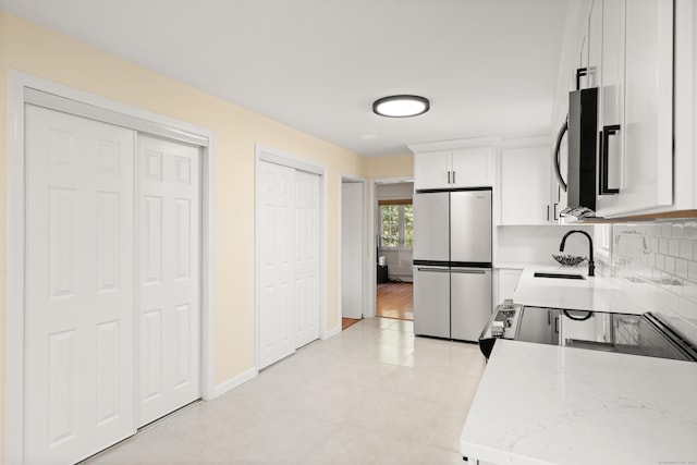 kitchen with baseboards, freestanding refrigerator, a sink, white cabinetry, and tasteful backsplash