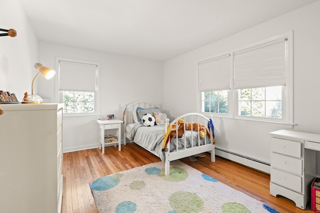 bedroom with a baseboard heating unit and light wood-style floors