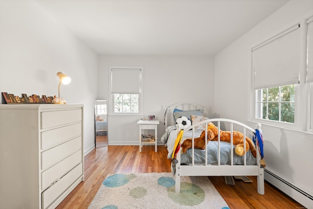 bedroom with light wood-style floors, baseboards, and baseboard heating