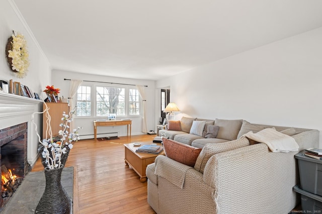 living room with a brick fireplace, a baseboard heating unit, light wood-style floors, and crown molding