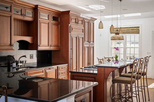 kitchen featuring a skylight, a sink, a kitchen bar, dark countertops, and backsplash