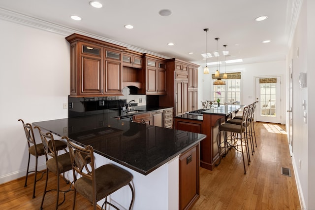 kitchen with visible vents, light wood-style flooring, a kitchen breakfast bar, dark countertops, and crown molding