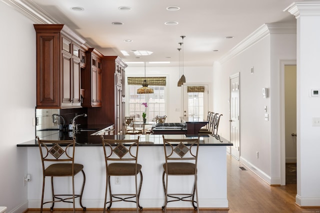 kitchen featuring pendant lighting, a kitchen breakfast bar, dark countertops, a peninsula, and light wood finished floors