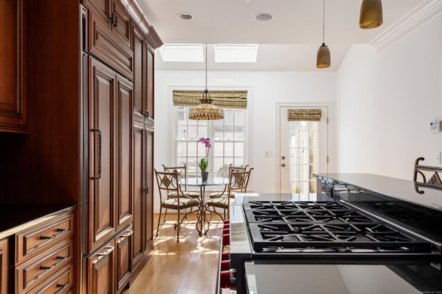 kitchen with paneled fridge, pendant lighting, light wood-style flooring, crown molding, and stainless steel range with gas stovetop