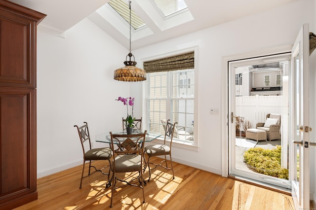 dining space with light wood-type flooring, vaulted ceiling with skylight, and baseboards