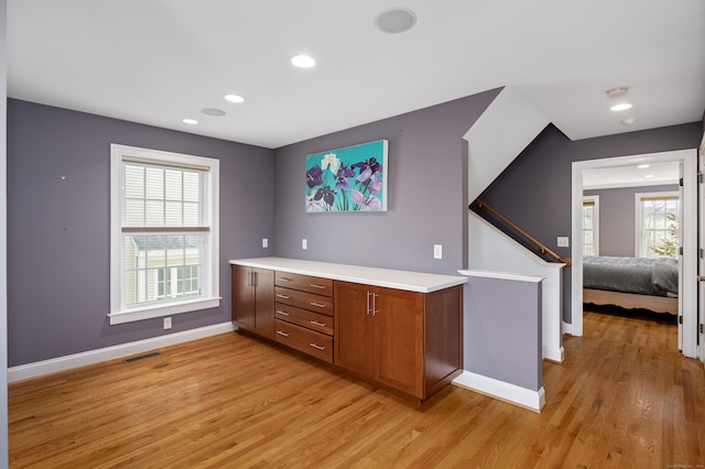 kitchen featuring brown cabinetry, visible vents, baseboards, light wood-style flooring, and light countertops