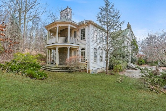 view of front of home with a chimney, a balcony, and a front lawn