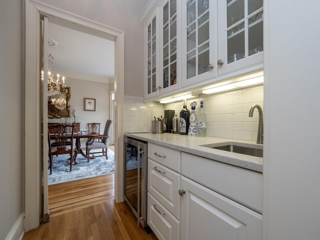 bar featuring wine cooler, wood finished floors, a sink, backsplash, and crown molding