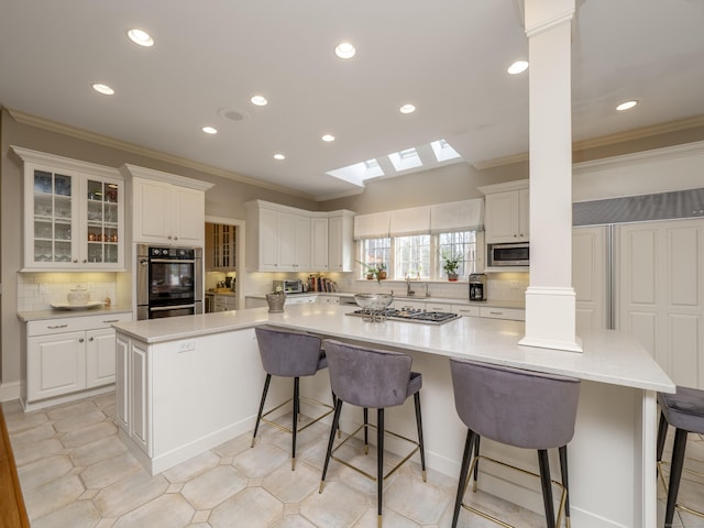 kitchen with a skylight, decorative columns, stainless steel appliances, a spacious island, and ornamental molding