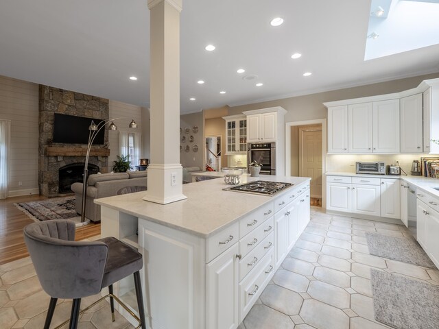 kitchen featuring stainless steel appliances, a fireplace, a kitchen island, white cabinetry, and ornate columns