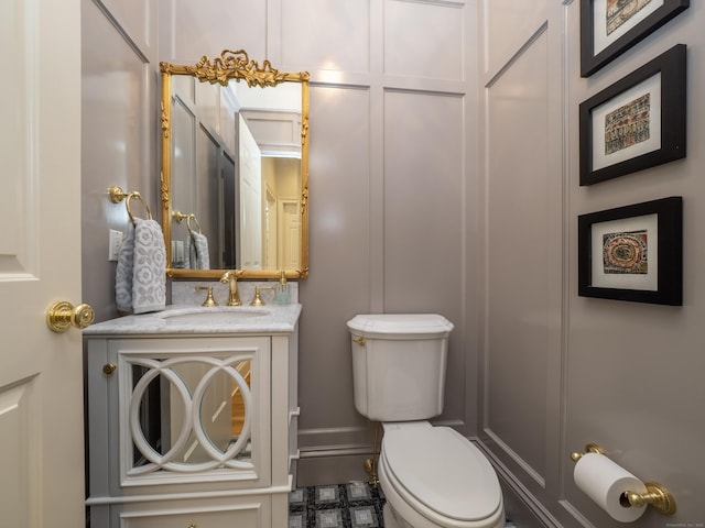 half bath featuring a decorative wall, vanity, and toilet