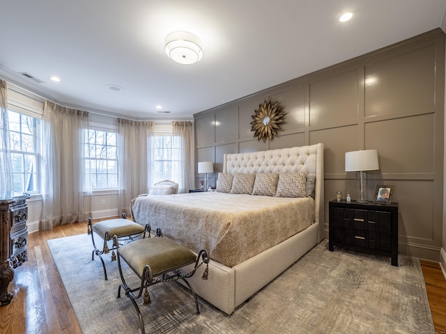 bedroom featuring multiple windows, a decorative wall, and wood finished floors