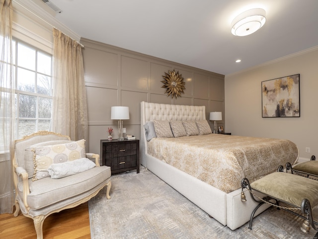 bedroom featuring crown molding, light wood-type flooring, visible vents, and a decorative wall