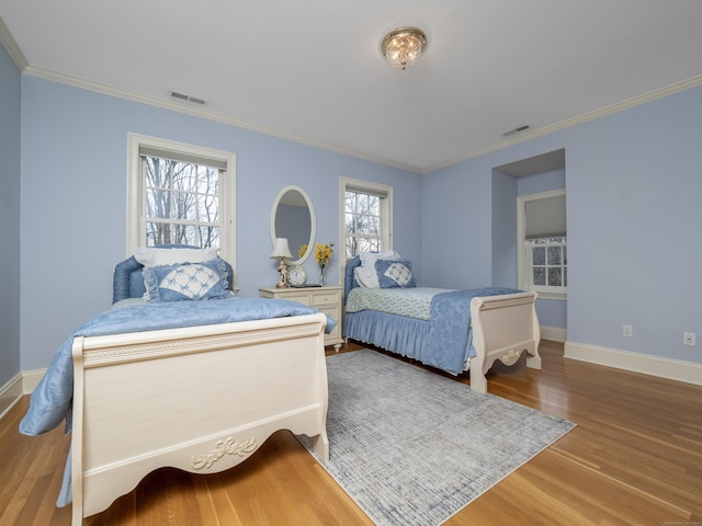 bedroom with baseboards, crown molding, visible vents, and wood finished floors