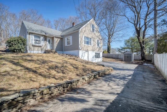 view of front of property featuring fence, a chimney, a storage shed, an outdoor structure, and driveway