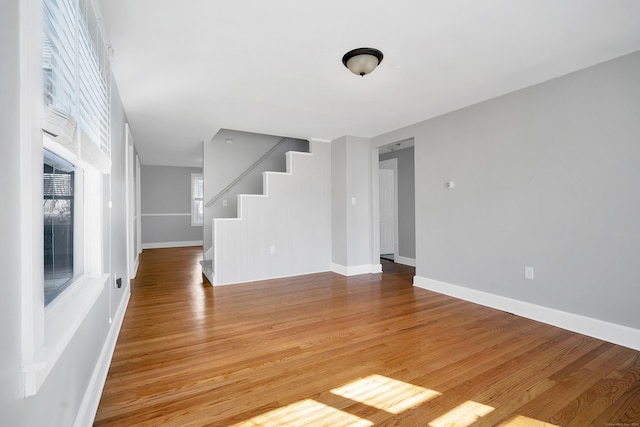 spare room featuring stairway, light wood-style flooring, and baseboards