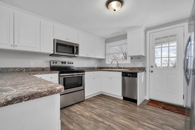 kitchen with a sink, dark countertops, dark wood-style floors, white cabinetry, and stainless steel appliances