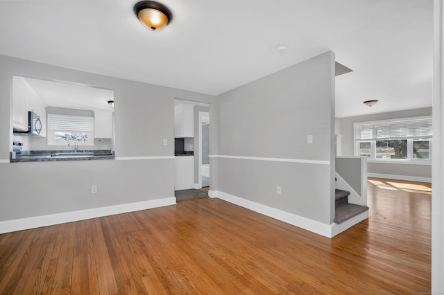 unfurnished living room featuring stairs, baseboards, and wood finished floors