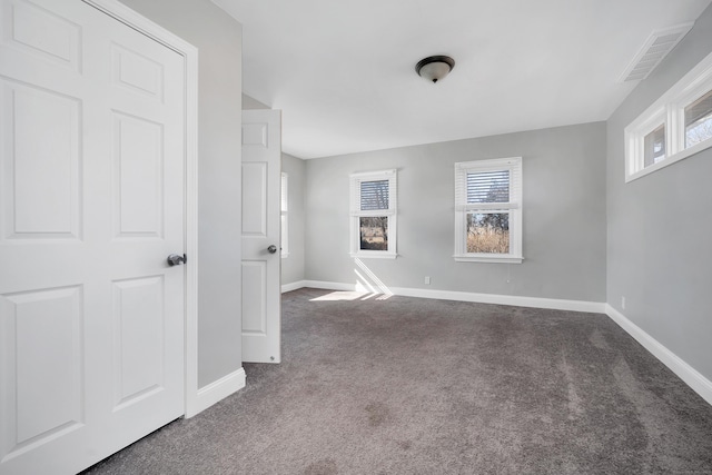 unfurnished room with dark colored carpet, visible vents, and baseboards