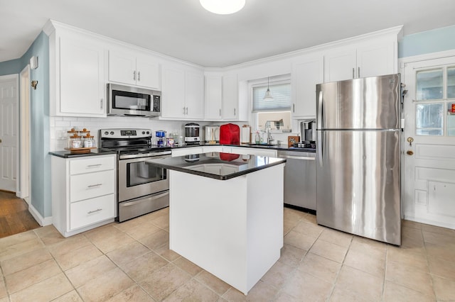 kitchen featuring stainless steel appliances, a kitchen island, white cabinetry, backsplash, and dark countertops