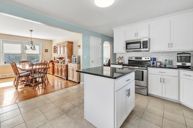 kitchen featuring a center island, arched walkways, dark countertops, decorative backsplash, and appliances with stainless steel finishes