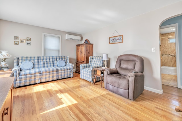 living area with arched walkways, a wall mounted air conditioner, light wood-style flooring, and baseboards