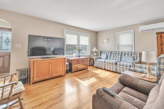 living room with arched walkways, a wall mounted air conditioner, and light wood-style floors