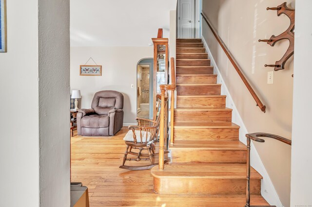 stairs featuring arched walkways and wood finished floors