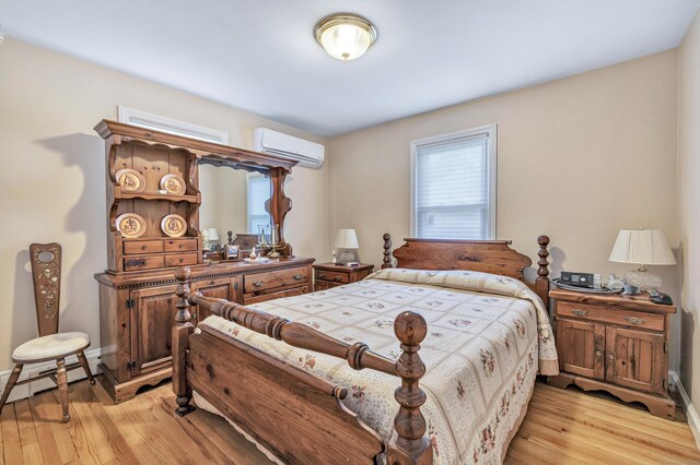 bedroom featuring light wood finished floors, baseboard heating, a wall mounted air conditioner, and baseboards