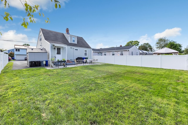 back of house featuring a fenced backyard, a shingled roof, a yard, a chimney, and a patio area