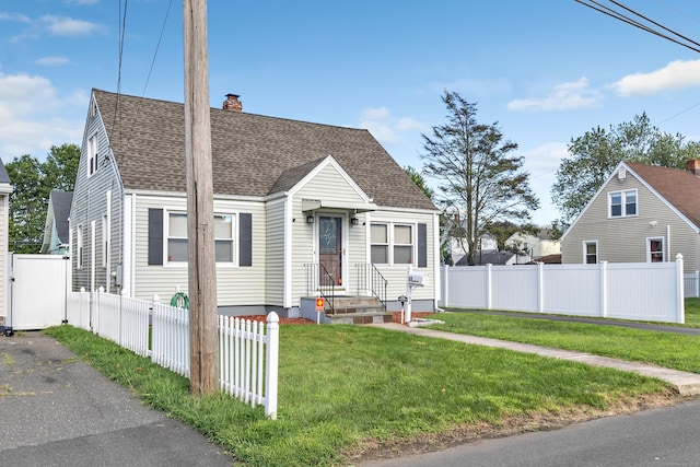 view of front facade with a shingled roof, a chimney, a front yard, and fence private yard