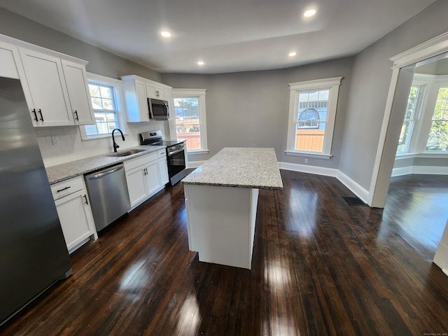 kitchen with stainless steel appliances, dark wood-style flooring, a kitchen island, a sink, and baseboards