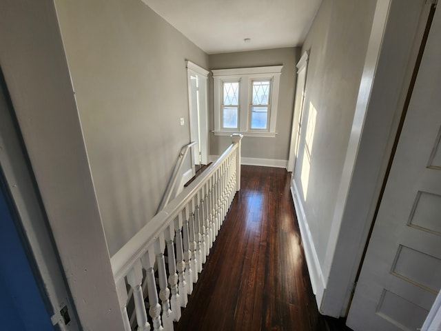 hallway featuring baseboards, dark wood-style flooring, and an upstairs landing