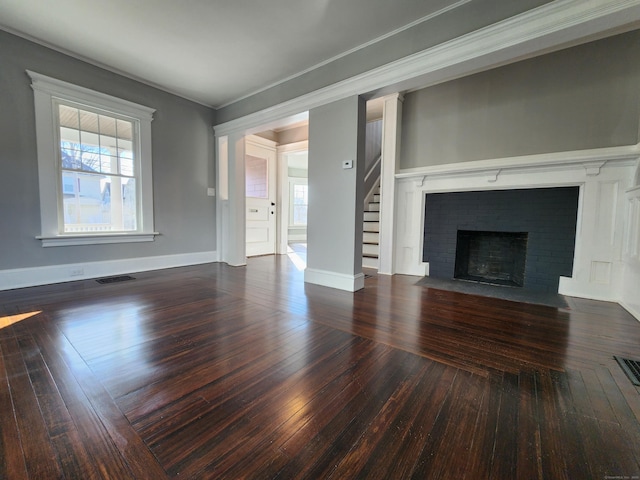 unfurnished living room featuring visible vents, baseboards, hardwood / wood-style floors, stairs, and a brick fireplace