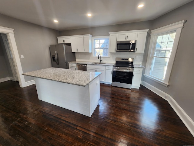 kitchen with a kitchen island, a sink, baseboards, appliances with stainless steel finishes, and dark wood-style floors