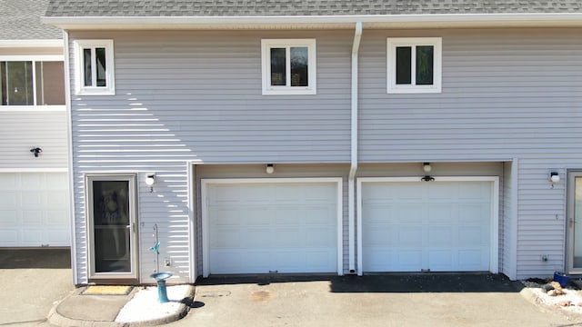 back of property with an attached garage, mansard roof, driveway, and roof with shingles