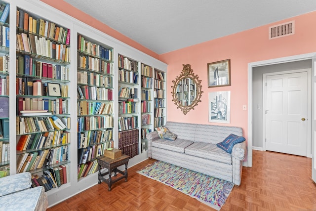 sitting room with a textured ceiling, bookshelves, and visible vents