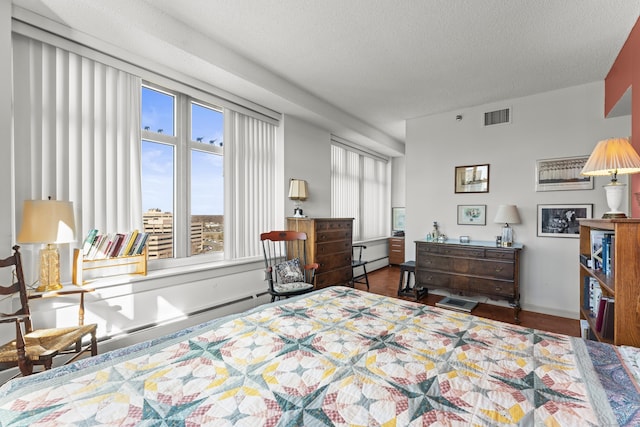 bedroom featuring baseboards, visible vents, wood finished floors, baseboard heating, and a textured ceiling