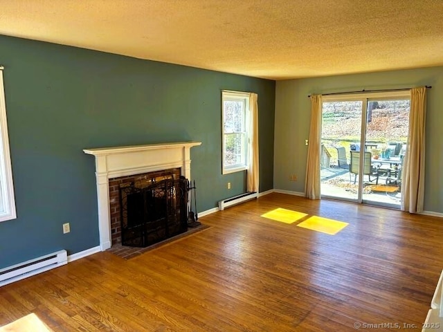 unfurnished living room with a baseboard heating unit, wood finished floors, a fireplace with flush hearth, and baseboards