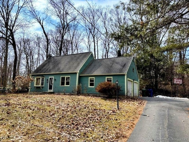 cape cod house with aphalt driveway, a chimney, and an attached garage