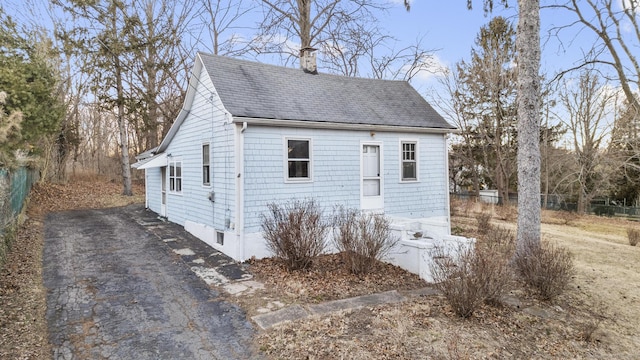 exterior space with a shingled roof, a chimney, fence, and aphalt driveway