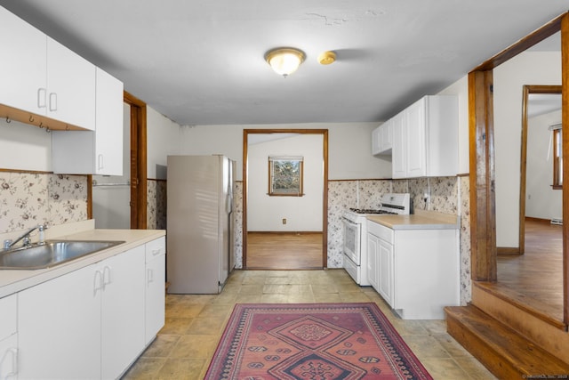 kitchen with white appliances, light countertops, a sink, and white cabinetry