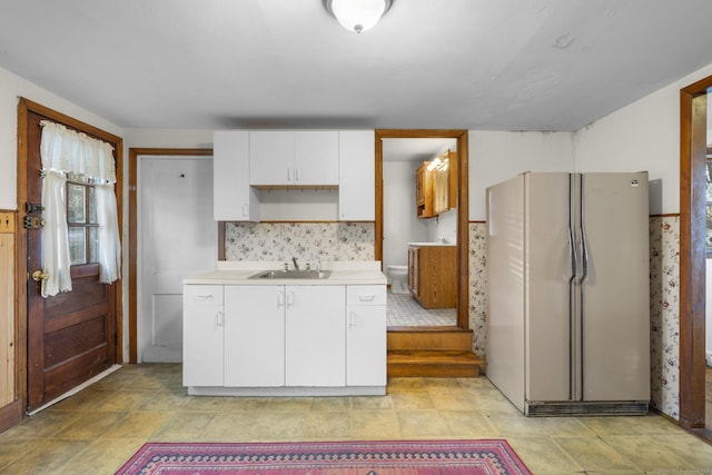 kitchen featuring tasteful backsplash, white cabinets, freestanding refrigerator, light countertops, and a sink