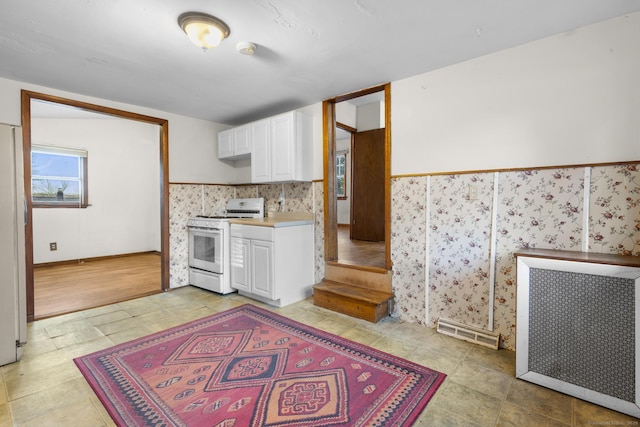 kitchen featuring white gas stove, a wainscoted wall, white cabinets, light countertops, and radiator heating unit