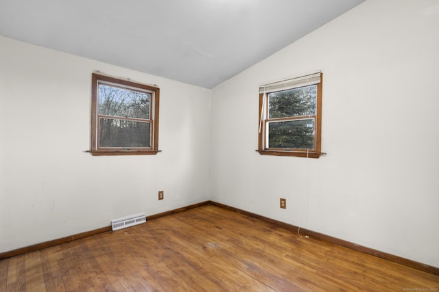 unfurnished room with a wealth of natural light, visible vents, vaulted ceiling, and hardwood / wood-style floors