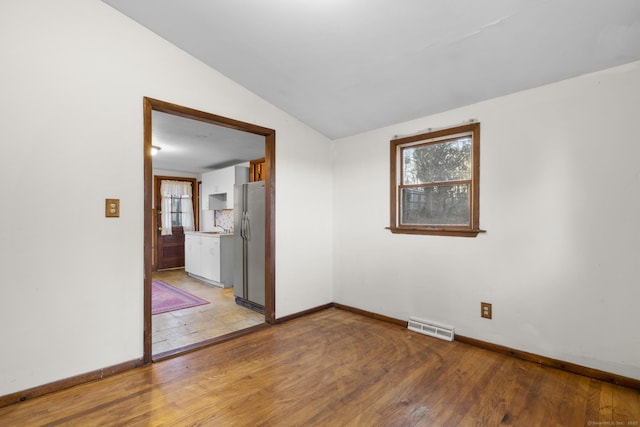 empty room with a healthy amount of sunlight, visible vents, vaulted ceiling, and light wood-style flooring